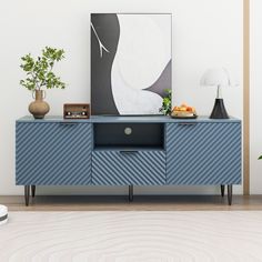 a blue sideboard with a painting on the wall next to a lamp and potted plant