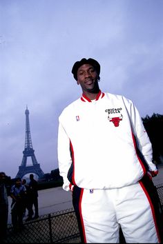 a man standing in front of the eiffel tower wearing a white and red jacket