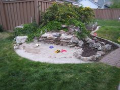 a backyard area with rocks and flowers in the yard, including a sand pit for children to play in