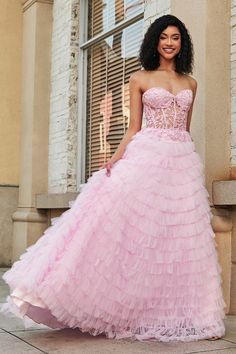 a woman in a pink dress is standing on the sidewalk near a building and smiling