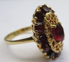 This ring looks so regal! The deep red garnets against the rich colored 18k gold compliment each other beautifully. Dating from the early 1900's-40's and hallmarked in the interior 750 and 176AAL. Has been tested to ensure the golds purity. Rings size is 6 1/2 and is ready to be worn and admired! The halo setting measures 11/16 by 7/16 of an inch. Stones are all held securely in place. Center garnet measures 6.12mm by 4.25mm. Some stones have light surface wear as to be expected with a ring of s Elegant Garnet Ruby Ring Stamped 14k, Victorian Ruby Rings In Yellow Gold, Victorian Yellow Gold Rings With Ruby, Victorian Ruby Ring In Yellow Gold, Victorian Yellow Gold Ruby Ring With Intricate Design, Victorian Ruby Ring In Yellow Gold With Intricate Design, Heirloom Gold Garnet Rings, Vintage Garnet Ruby Ring With Intricate Design, Vintage Multi-stone Ruby Ring