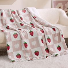 a blanket with strawberries on it is sitting on a couch next to a white chair