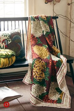 a chair with a blanket on it in front of a window and some pillows next to it