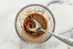 a spoon in a glass bowl filled with brown sauce and sesame seeds on a marble counter top