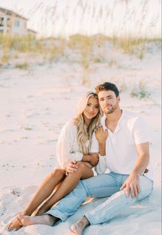 a man and woman are sitting in the sand on the beach with their arms around each other