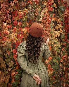 a woman with long hair standing in front of a wall covered in colorful leaves and ivys