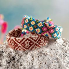 two bracelets sitting on top of a rock next to each other with beaded designs