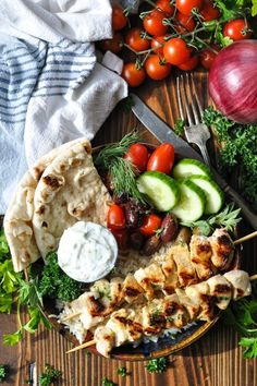 chicken skewers with vegetables and pita bread on a wooden table next to a fork