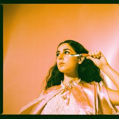 a woman brushing her hair with an electric toothbrush in front of a pink wall