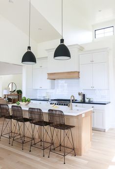 a kitchen with white cabinets and black pendant lights hanging from the ceiling over the island