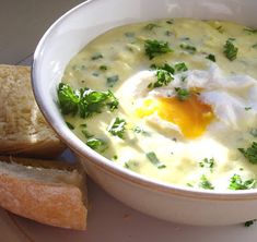 a bowl of soup with an egg in it next to some bread on a plate