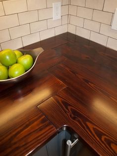 a bowl filled with green apples on top of a wooden counter