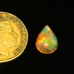 a small piece of gold next to an opalite on a black background with a coin in the foreground