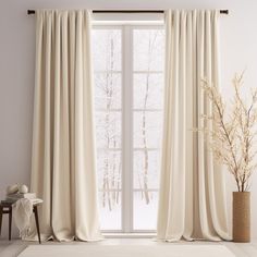 a living room with a large window covered in white curtains and a vase filled with flowers