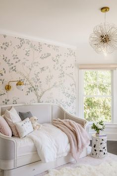 a white day bed sitting in a bedroom next to a window with a chandelier