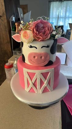 a pink and white cake with a cow face on it's side, decorated with flowers