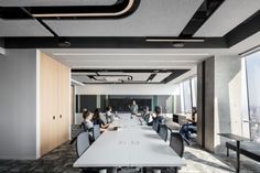 an office with people sitting at long tables in front of large windows looking out on the city