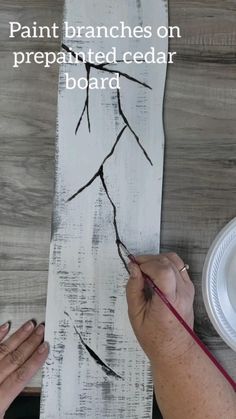 someone is painting branches on a piece of wood