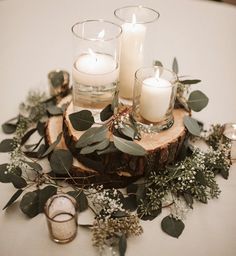 candles and greenery are arranged on a wood slice