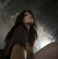 a woman sitting on the ground with her eyes closed and fireworks in the sky behind her