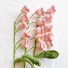 crocheted pink flowers with green stems on a white cloth covered tablecloth or wall hanging