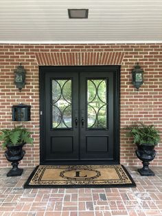 a black double door with two planters on either side and a welcome mat in front