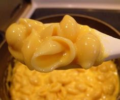 a spoon full of macaroni and cheese is being held over the stove top