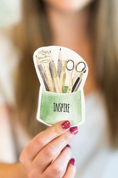 a woman holding up a cup with scissors and pens in it that says inspire inside