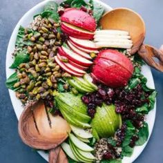 a white plate topped with sliced apples and other fruits next to wooden spoons on top of a table