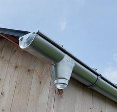 a metal gutter on the side of a wooden building with a sky background and clouds