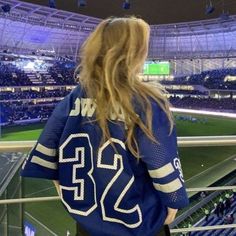 a woman in a blue jersey is looking out at the stadium and stands with her back to the camera