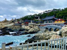 a bridge over the ocean next to some rocks and buildings on top of it,