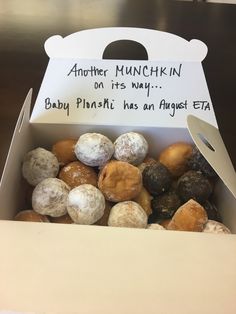 a box filled with assorted donuts sitting on top of a wooden table next to a sign that says another munchin on it's way