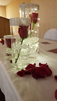 three vases with roses in them sitting on a white tableclothed table cloth