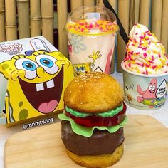 a spongebob burger next to two ice creams on a wooden board with strawberries and sprinkles in the background