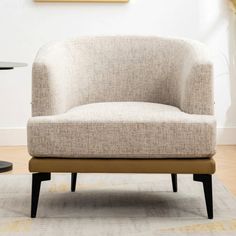 a beige chair sitting on top of a wooden floor next to a table and lamp