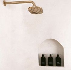 a shower head with three bottles on the wall and soap dispensers below it