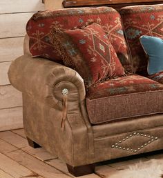 a brown couch with pillows on top of it next to a wooden floor and wall