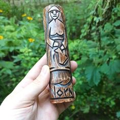 a hand holding a carved wooden object in front of some trees and bushes with wildflowers