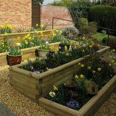 a garden filled with lots of flowers next to a brick wall and wooden planters