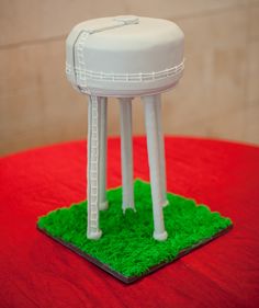 a cake shaped like a water tower sitting on top of a green patch of grass