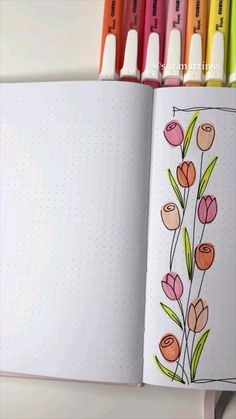 an open notebook with markers on it and flowers drawn in pencils next to it