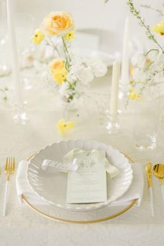 the table is set with white and gold plates, silverware, and yellow flowers