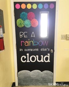 a door decorated with paper flowers and the words be a rainbow in someone else's cloud