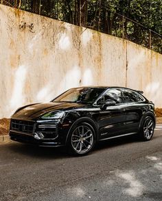 a black porsche cayen is parked on the side of the road in front of a wall