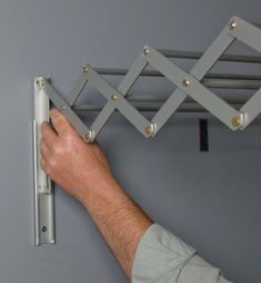 a hand is holding the handle on a wall mounted shelf with metal bars attached to it