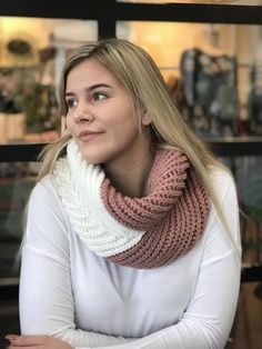 a woman sitting at a table with her arms crossed wearing a knitted cowl