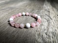 a pink and white beaded bracelet sitting on top of a wooden table