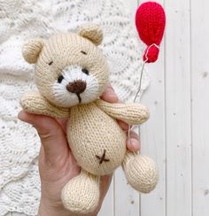 a hand holding a teddy bear with a red balloon