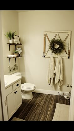 a white toilet sitting in a bathroom next to a wooden shelf filled with wreaths